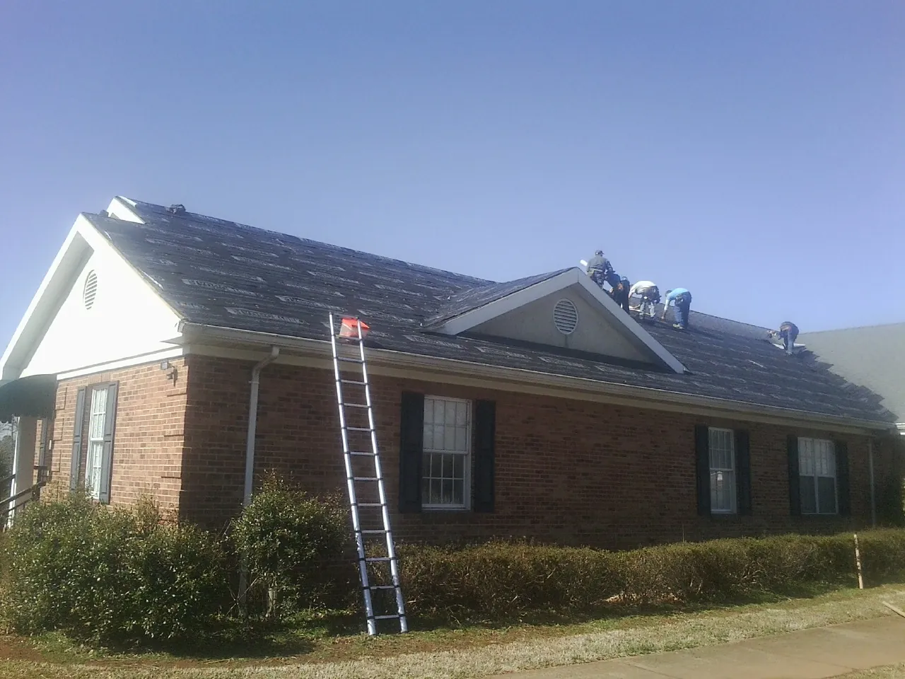 Crew tearing shingles off a brick ranch roof with a ladder set — Metal Roof Repair work by our crew in Steeles Tavern