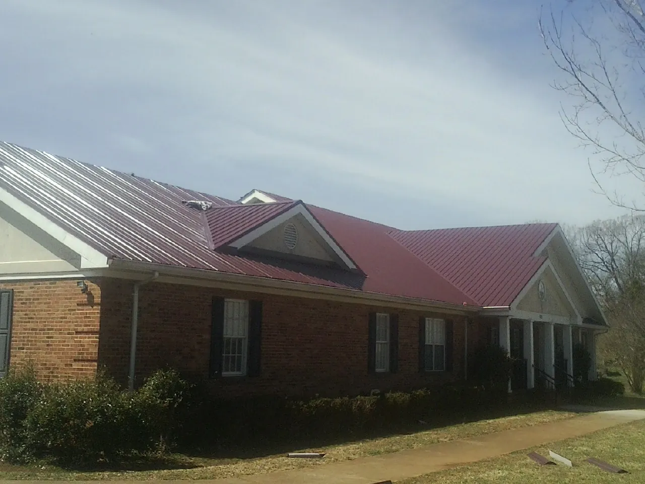 Red metal roof with gabled entries on a long brick building, from a Hail Damage Roof Repair job in Steeles Tavern