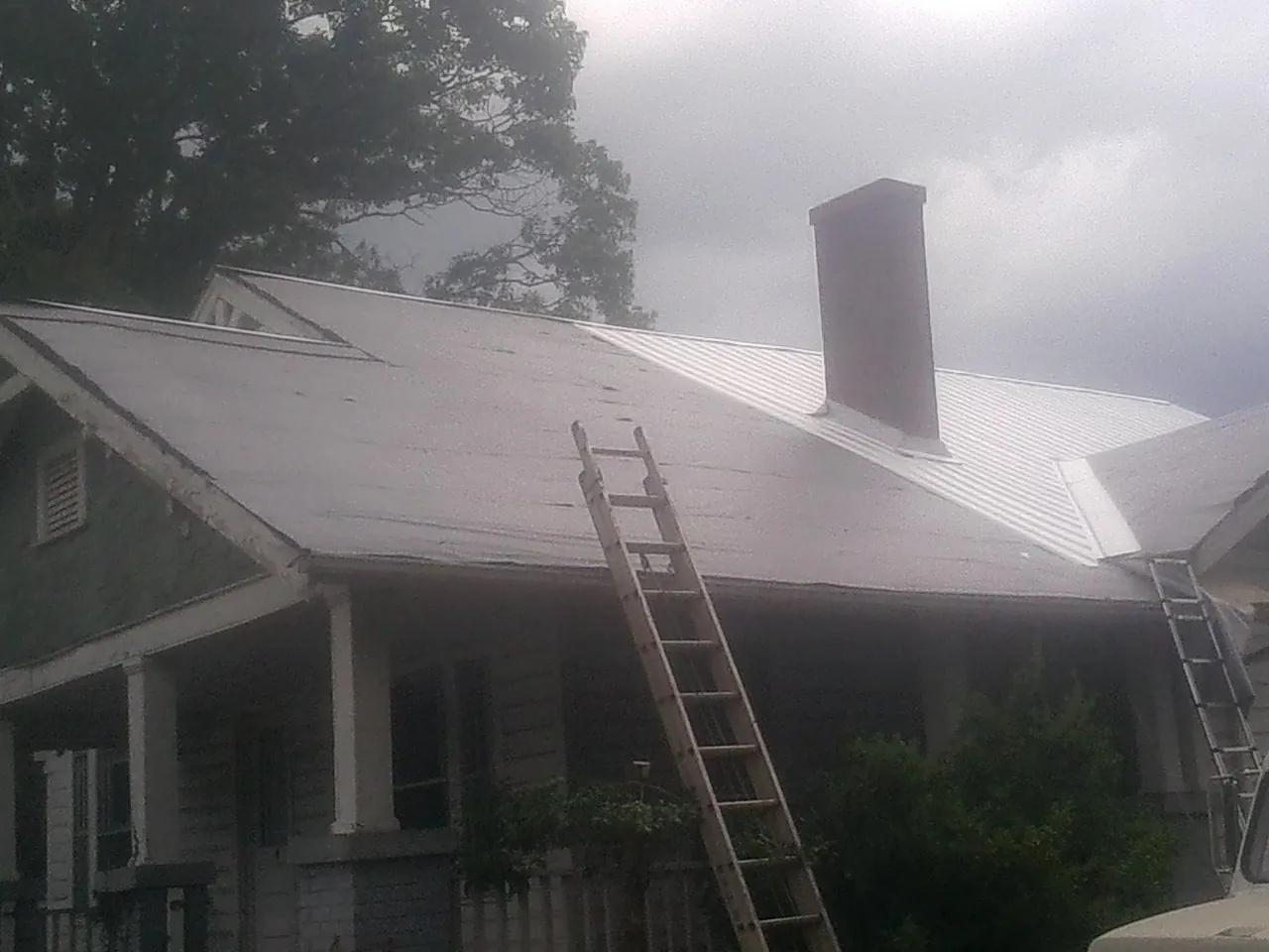 Ladders against a metal roof on an older home with a brick chimney in Steeles Tavern