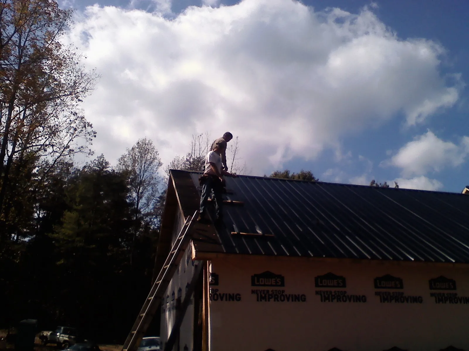 Roofer fastening dark metal panels high against a cloudy sky, from a Roof Inspection job in Steeles Tavern