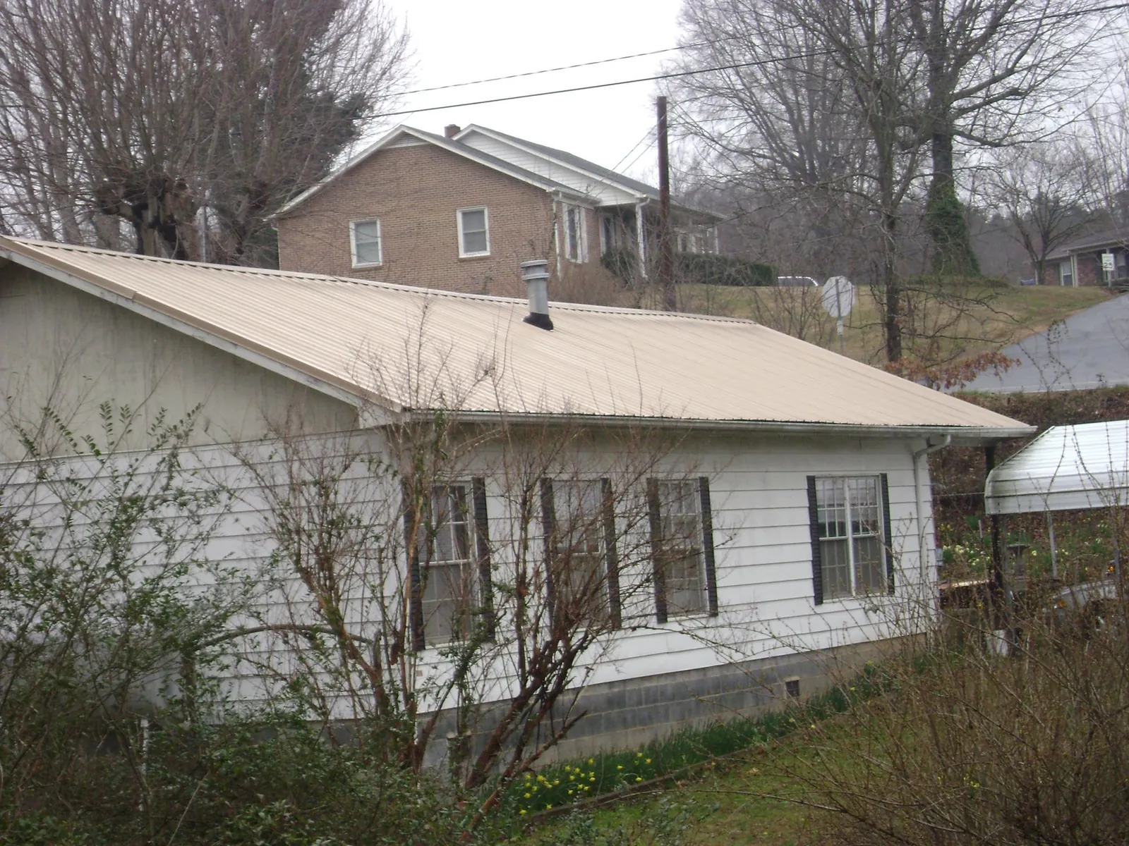 Tan metal roof on a white sided house set into a hillside — Commercial Roofing by Roofing Brothers in Steeles Tavern